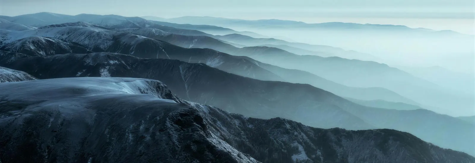 Rank after rank of mountain ridgelines receding into pale haze at blue hour