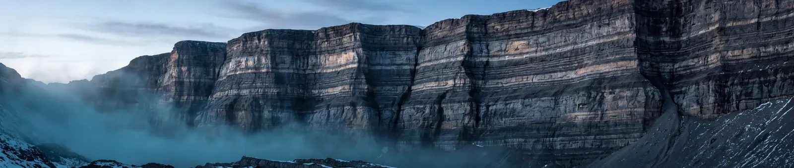 A wall of horizontally stratified alpine rock at first light, dozens of parallel layers picked out by low raking sun
